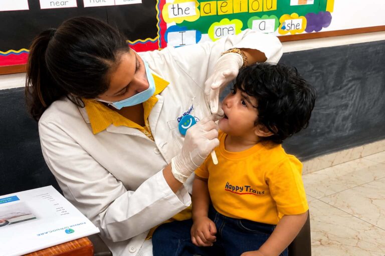 Pediatric dental checkup in a school classroom, with a dentist examining a child's oral health as part of a preventive dental care and oral hygiene awareness program.